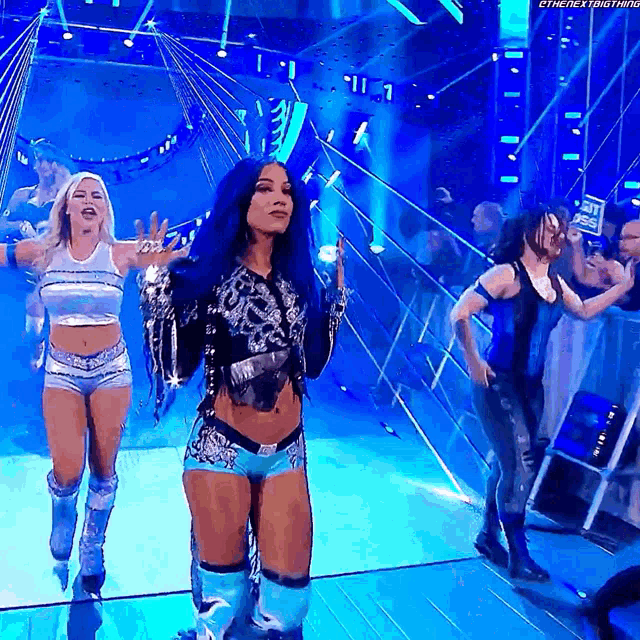 a woman with blue hair is walking on a stage with other women