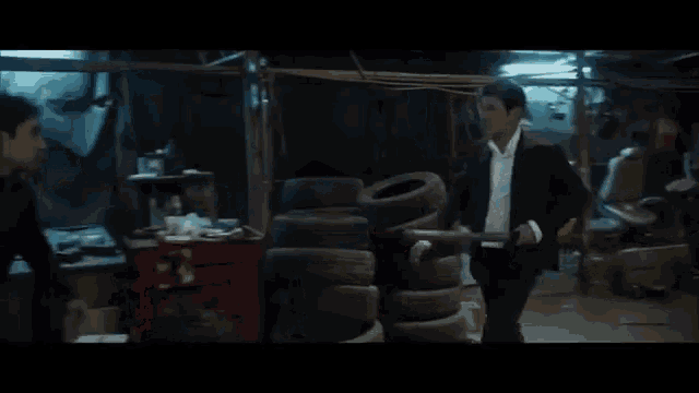 a man in a suit and white shirt is holding a sword in a dark room