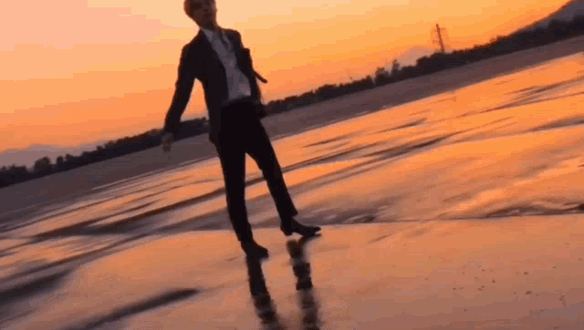 a man in a suit and tie is standing on a beach at sunset .