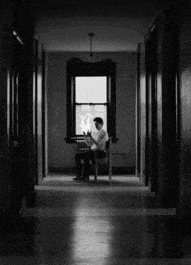 a man sits in a chair in a hallway looking out of a window