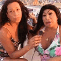 two women in bikinis are sitting on a boat drinking wine .