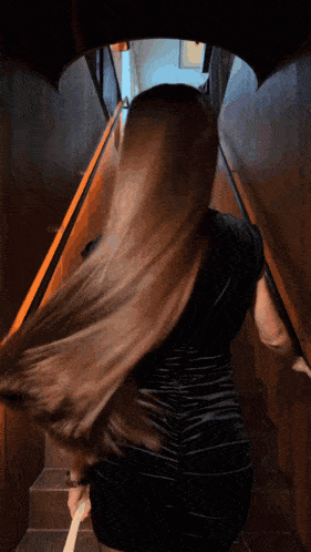 a woman in a black dress is walking down a set of stairs
