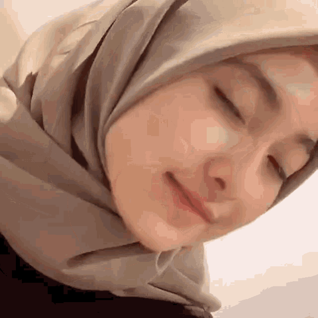 a woman in a hijab is smiling with her eyes closed .