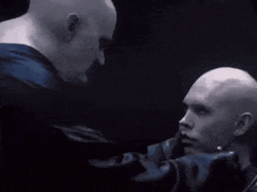 a bald man is holding another bald man in a dark room .