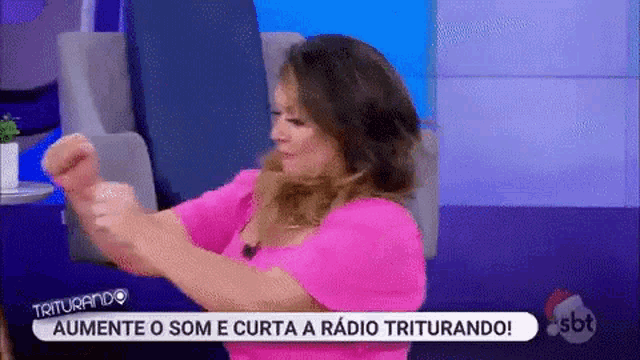 a woman in a pink shirt is making a fist while sitting on a couch .