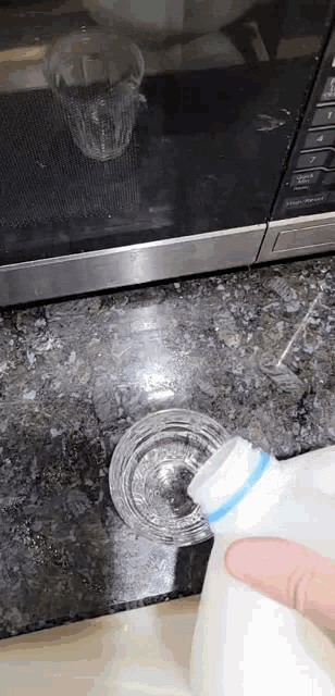 a person is pouring milk into a glass on a counter .