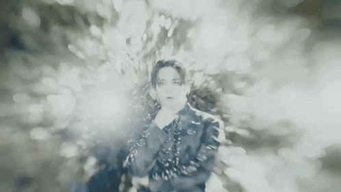 a black and white photo of a man in a black jacket standing in front of a blurred background .