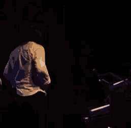 a man in a white shirt is playing a piano in the dark