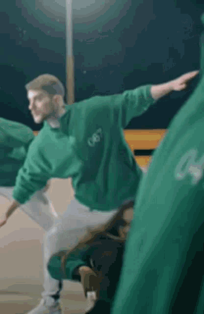 a man in a green sweatshirt is dancing in front of a crowd .