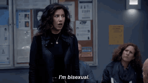 a woman is standing in front of a group of people in a room and saying i 'm bisexual .