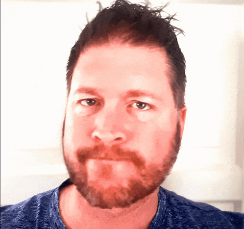 a man with a beard and a blue shirt is looking at the camera