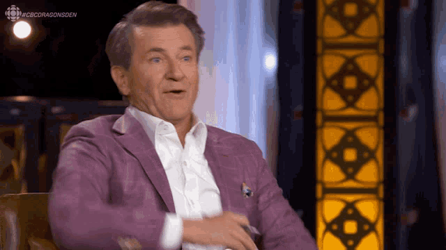 a man in a purple suit is sitting in front of a cbs dragonsoen sign
