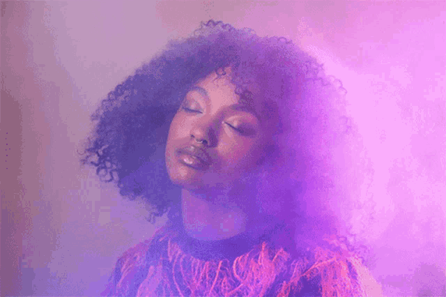 a woman with curly hair is surrounded by purple smoke with her eyes closed