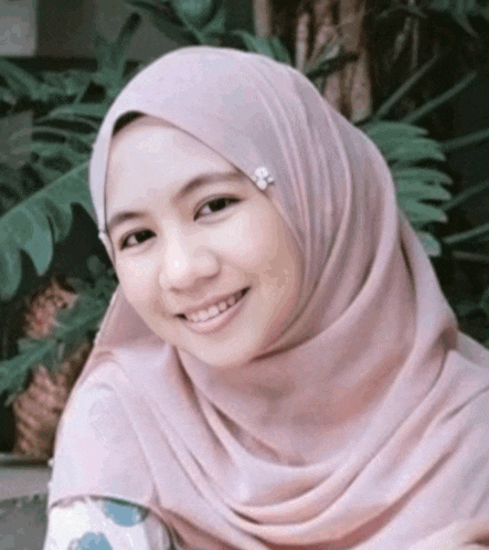 a woman wearing a pink hijab is smiling and wearing a brooch