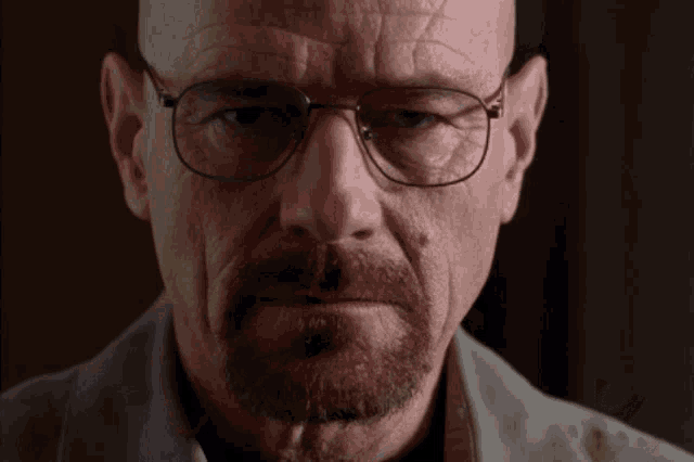 a man with glasses and a beard looks at the camera with a serious look on his face