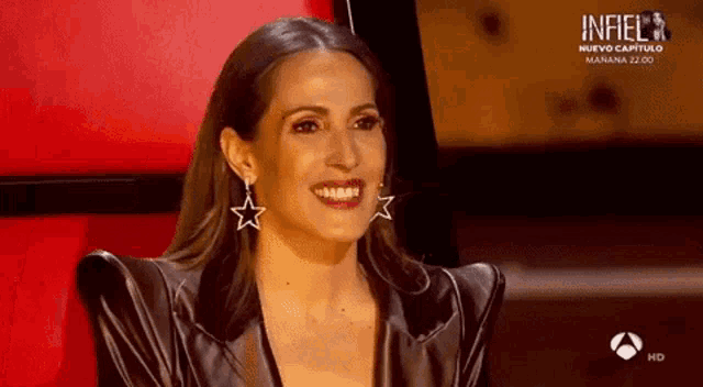 a woman wearing a black jacket and star earrings is smiling on a tv screen