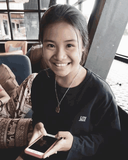 a girl wearing a black lite shirt smiles while holding a phone