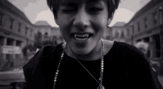 a young man with vampire teeth is wearing a black shirt and necklace