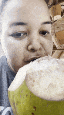a woman is eating a green coconut with a gray shirt on