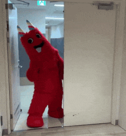 a red mascot is standing in a doorway with an exit sign above it