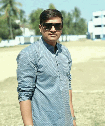 a man wearing sunglasses and a blue shirt is standing on a field