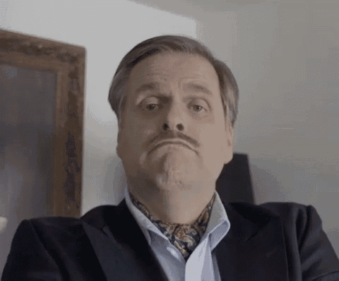 a man with a mustache is wearing a suit and tie and making a funny face .