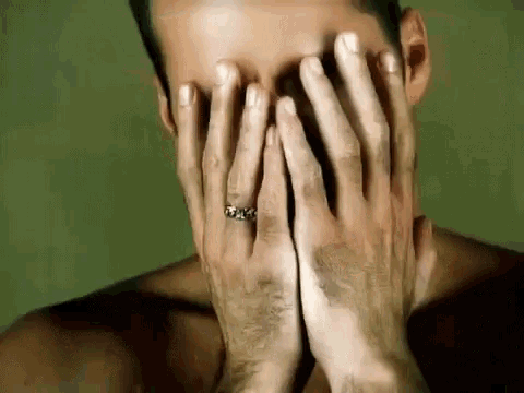 a shirtless man is covering his face with his hands while wearing a ring on his finger .