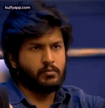 a man with a beard is looking at the camera while wearing a blue shirt .