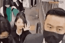 a man wearing a mask is waving at a woman in a crowd .