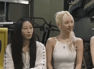 two women are sitting next to each other in a gym and one of them is wearing a white adidas tank top