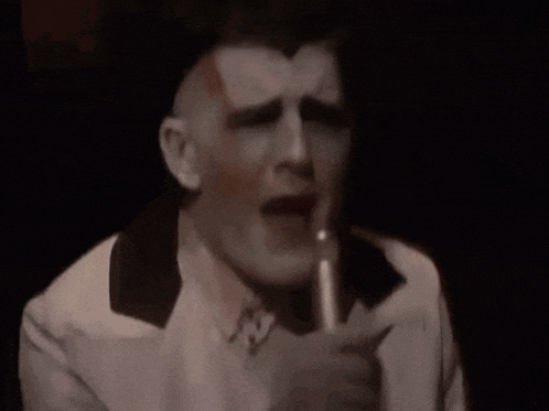 a man in a white suit is singing into a microphone in a dark room