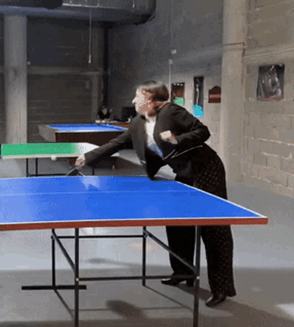 a woman in a suit is playing ping pong in a dark room
