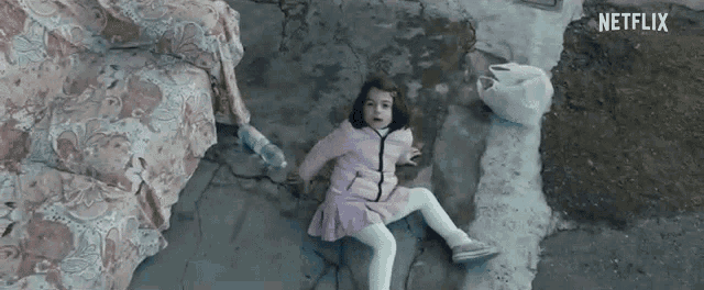 a little girl in a pink dress is laying on the ground in front of a netflix logo .