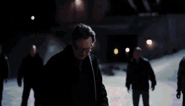 a man with glasses is standing in a dark room with a purple light behind him .