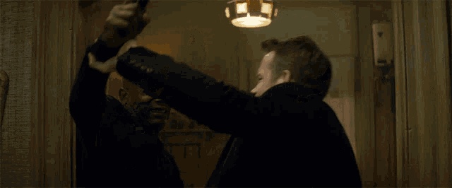 a man in a black suit is holding a knife while another man looks on