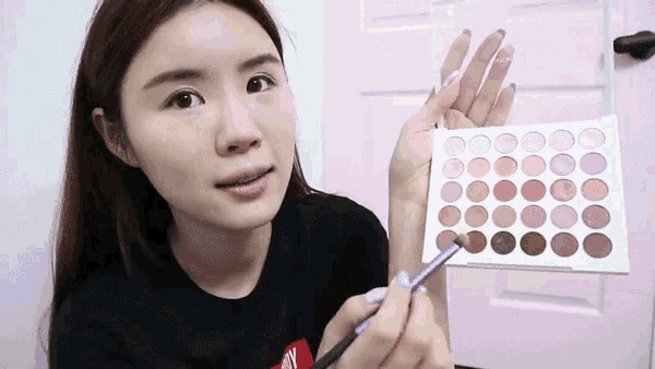 a woman is holding a makeup palette and a makeup brush