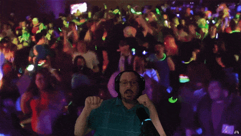 a man wearing headphones and glasses stands in front of a crowd of people