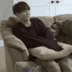 a man is sitting in a chair with a pillow on his lap