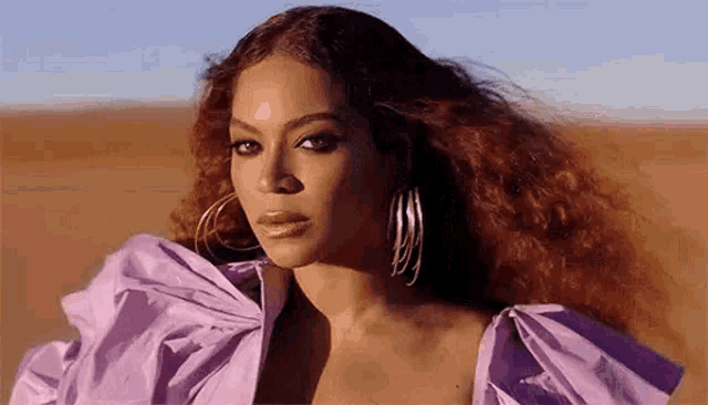 beyonce is wearing a purple dress and hoop earrings .