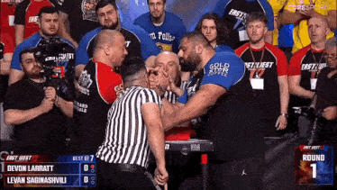 a group of men are watching a arm wrestling match between devon larratt and levan saginashvili