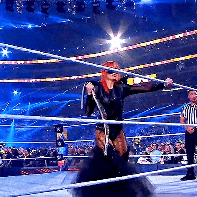 a woman in a black dress is standing in a wrestling ring with a referee behind her