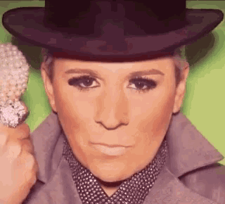 a woman wearing a top hat and a trench coat holds a pearl ring