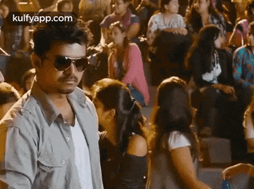 a man wearing sunglasses is standing in front of a crowd of people at a concert .