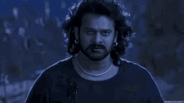 a man with long hair and a beard is standing in a dark forest