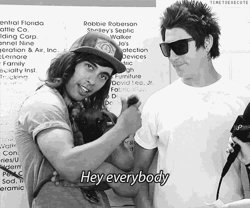 two men are standing next to each other and one of them is holding a dog and says hey everybody