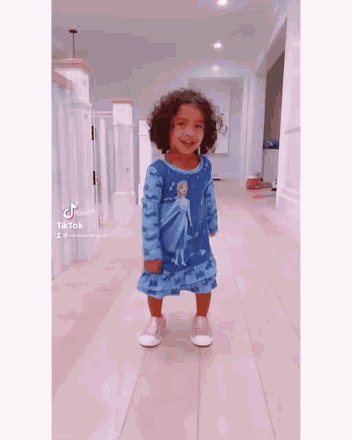 a little girl is standing in a hallway wearing a blue frozen dress .