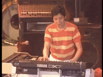 a man in a striped shirt is playing a yamaha cx7 keyboard