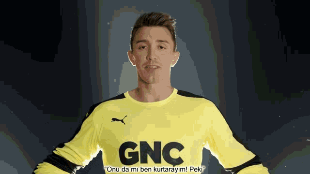 a man in a yellow gnc shirt stands in front of a dark background