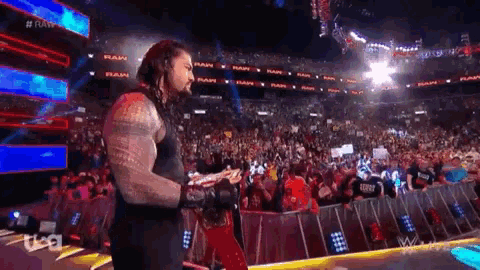 a wrestler is standing in front of a crowd in a stadium holding a belt .