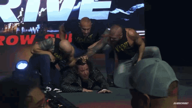 a group of men are wrestling in front of a large screen that says rive